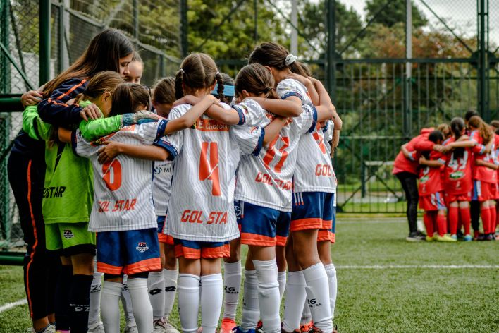 Young soccer team in white uniforms huddling on field, fostering teamwork.